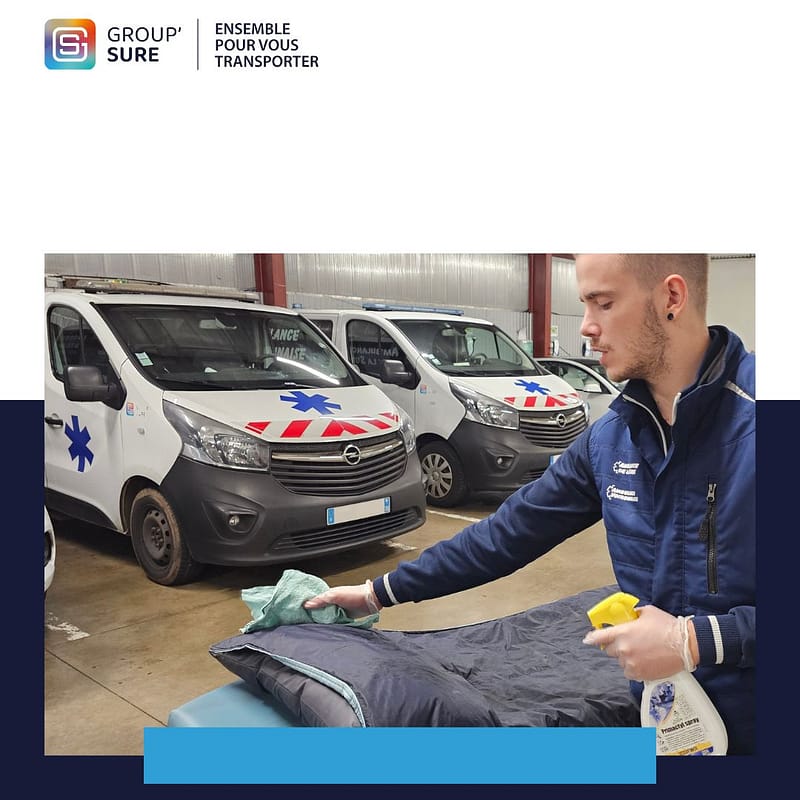 Un membre de Group’Sure nettoie et désinfecte le matériel d’un véhicule sanitaire dans un garage où plusieurs ambulances sont stationnées.